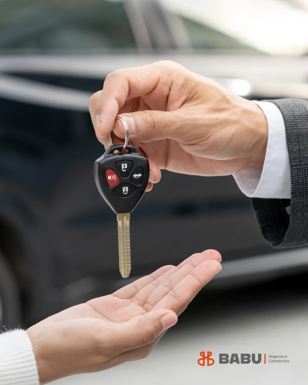 Mão entregando a chave de um carro para outra pessoa, com o carro ao fundo